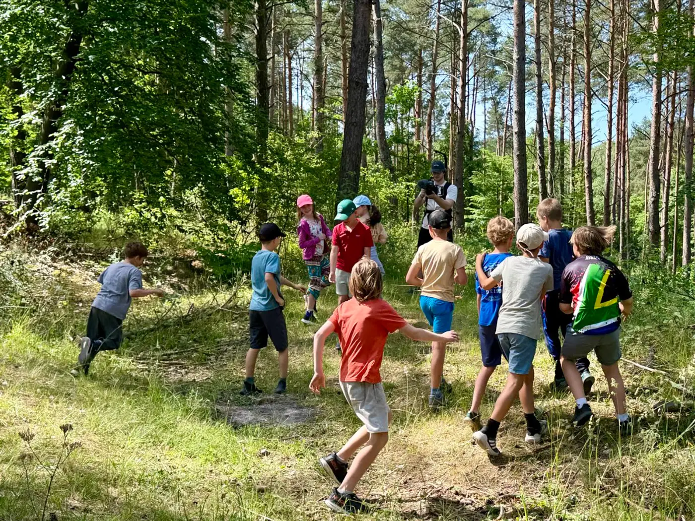 Grupa dzieci biegnie leśną ścieżką w głąb lasu, w stronę drzew.